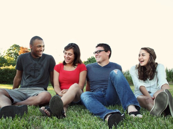 four people sitting in the grass and laughing