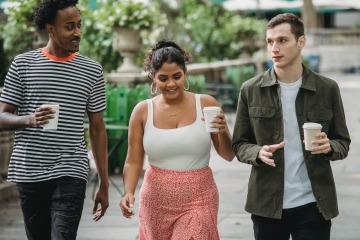 3 people walking, talking, and holding coffee in a park